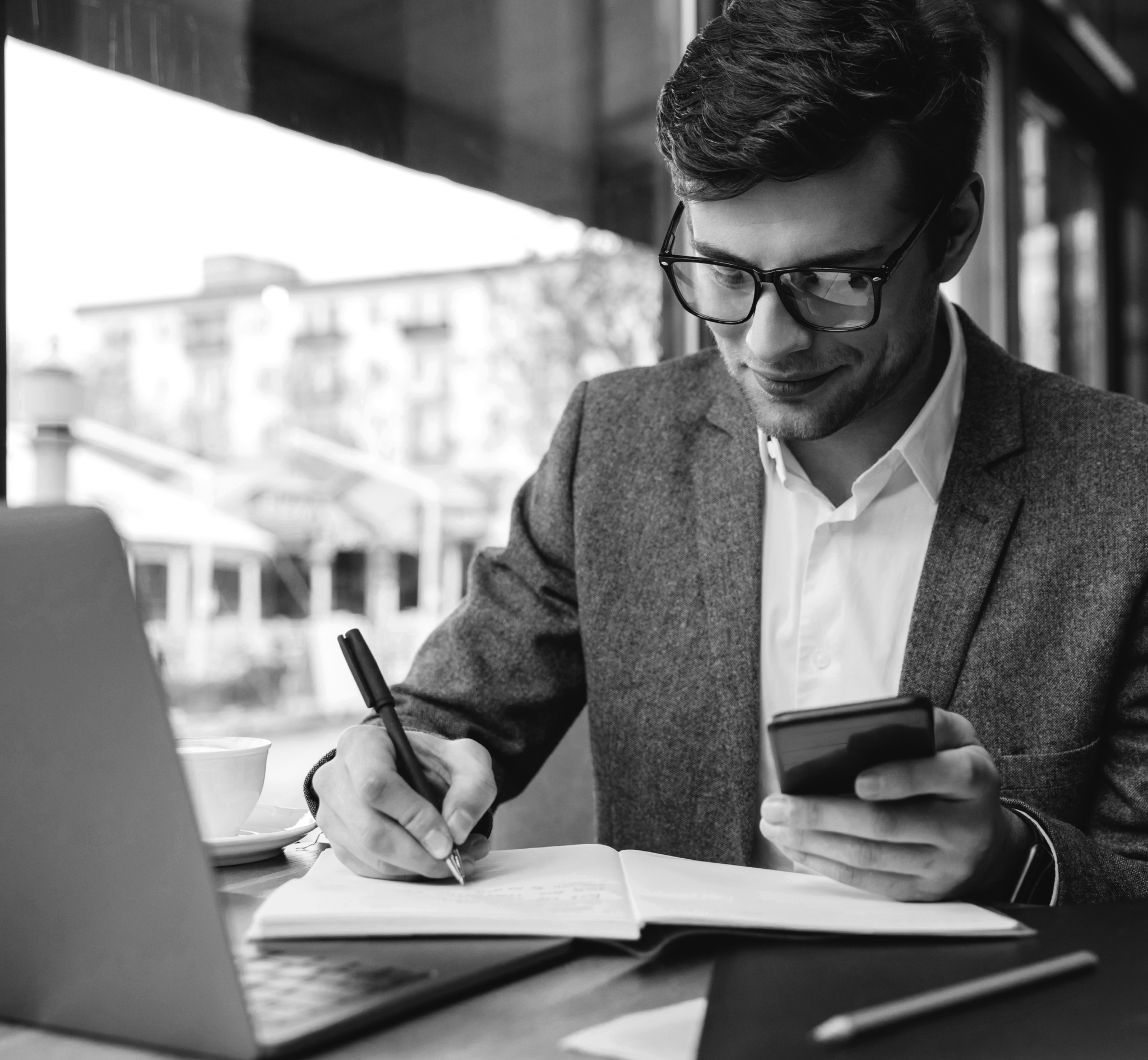 Image noir et blanc d'un comptable qui écrit sur un carnet avec son téléphone dans la main gauche